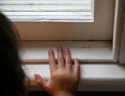 A child’s hand touching a painted window sill, highlighting the critical need to test for lead paint in areas accessible to children