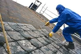 Worker in safety gear carefully removing asbestos shingles from roof